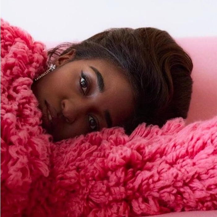 Editorial portrait resting on a pink shaggy knit, with sharply defined brows by Maggie Moon